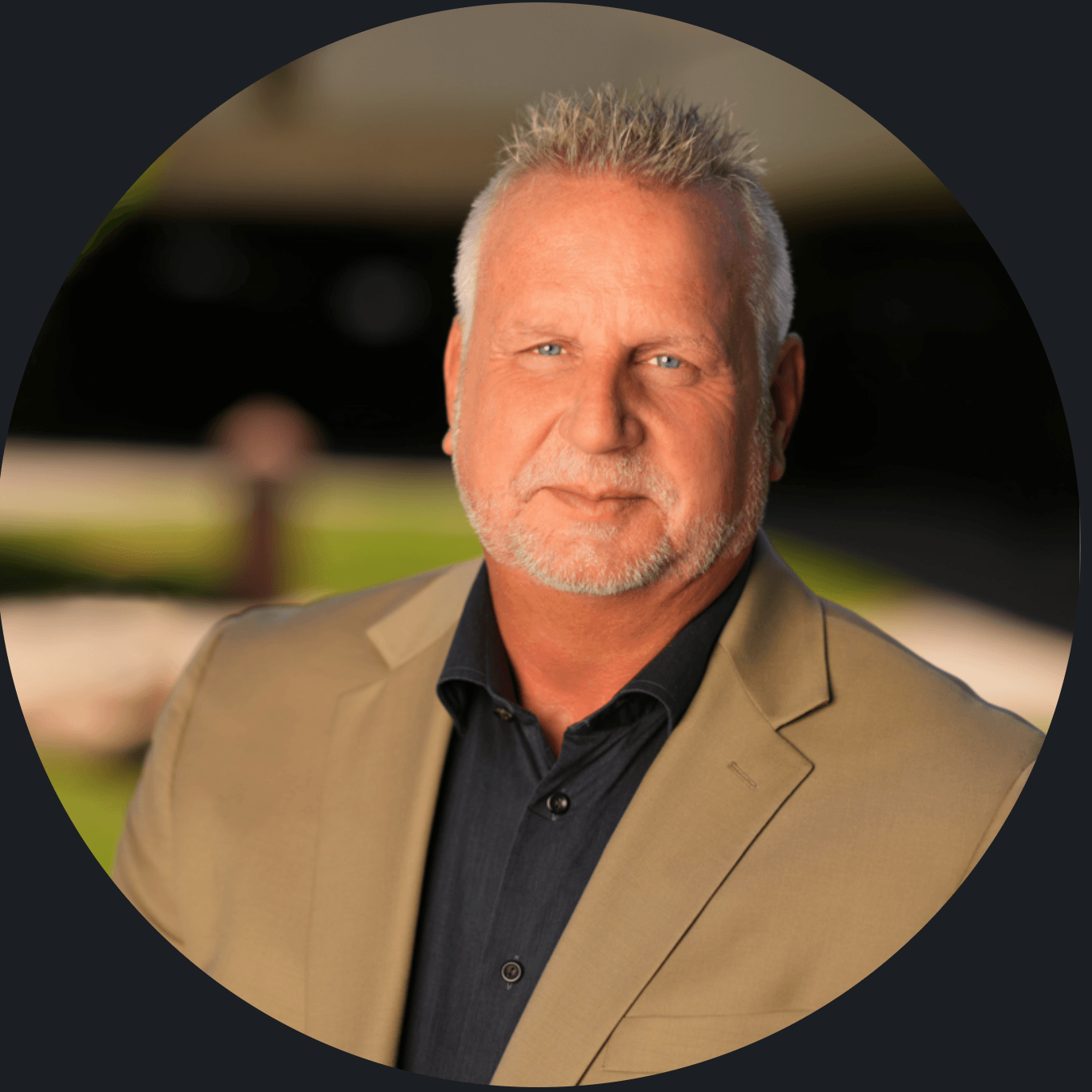 Professional headshot of Thad Russell in a black shirt and tan suit jacket