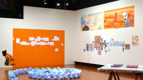 art installation featuring an orange wall and tumbled set of large dominoes