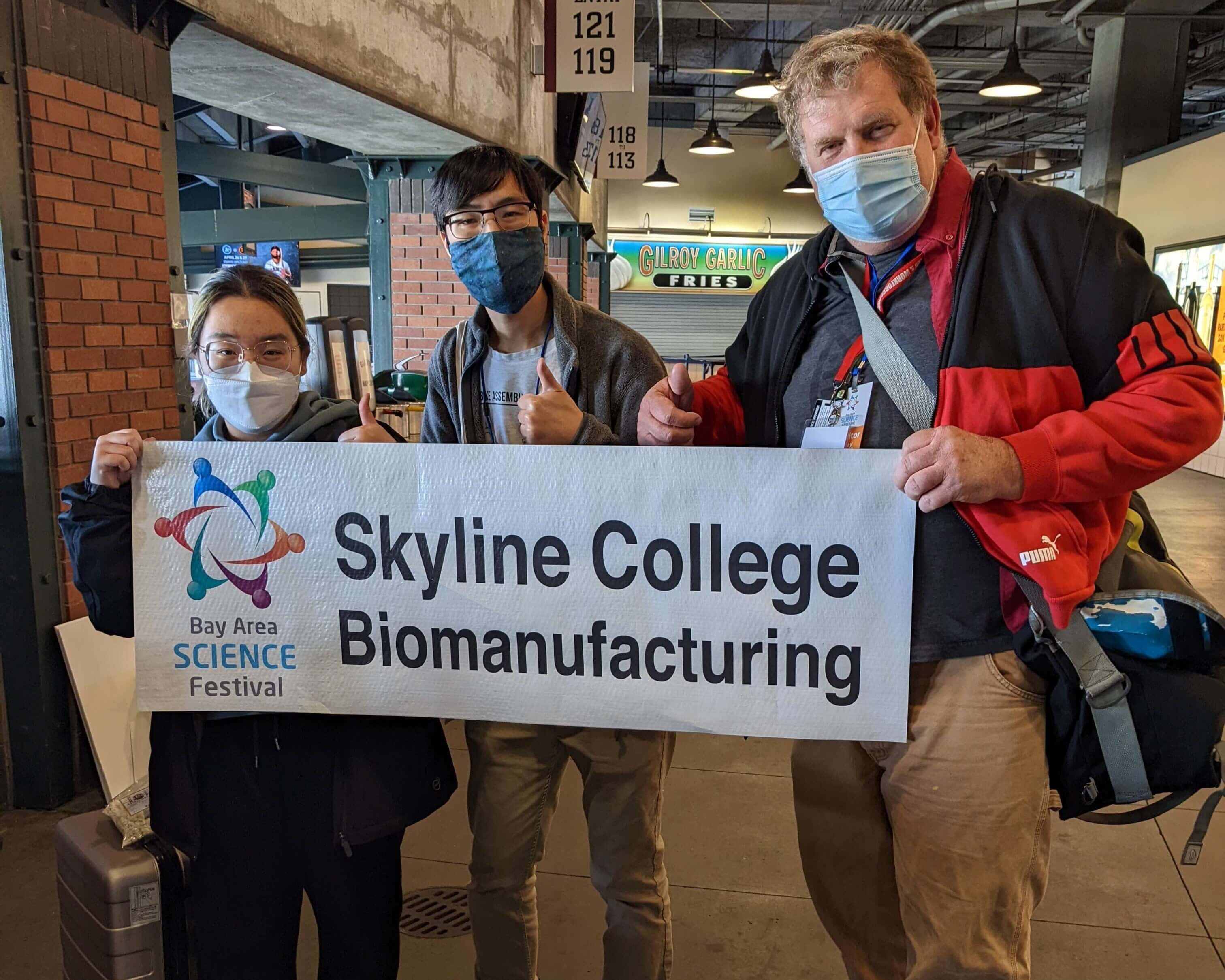 Faculty stand with a banner reading 'Skyline College Biomanufacturing' at the Bay Area Science Festival