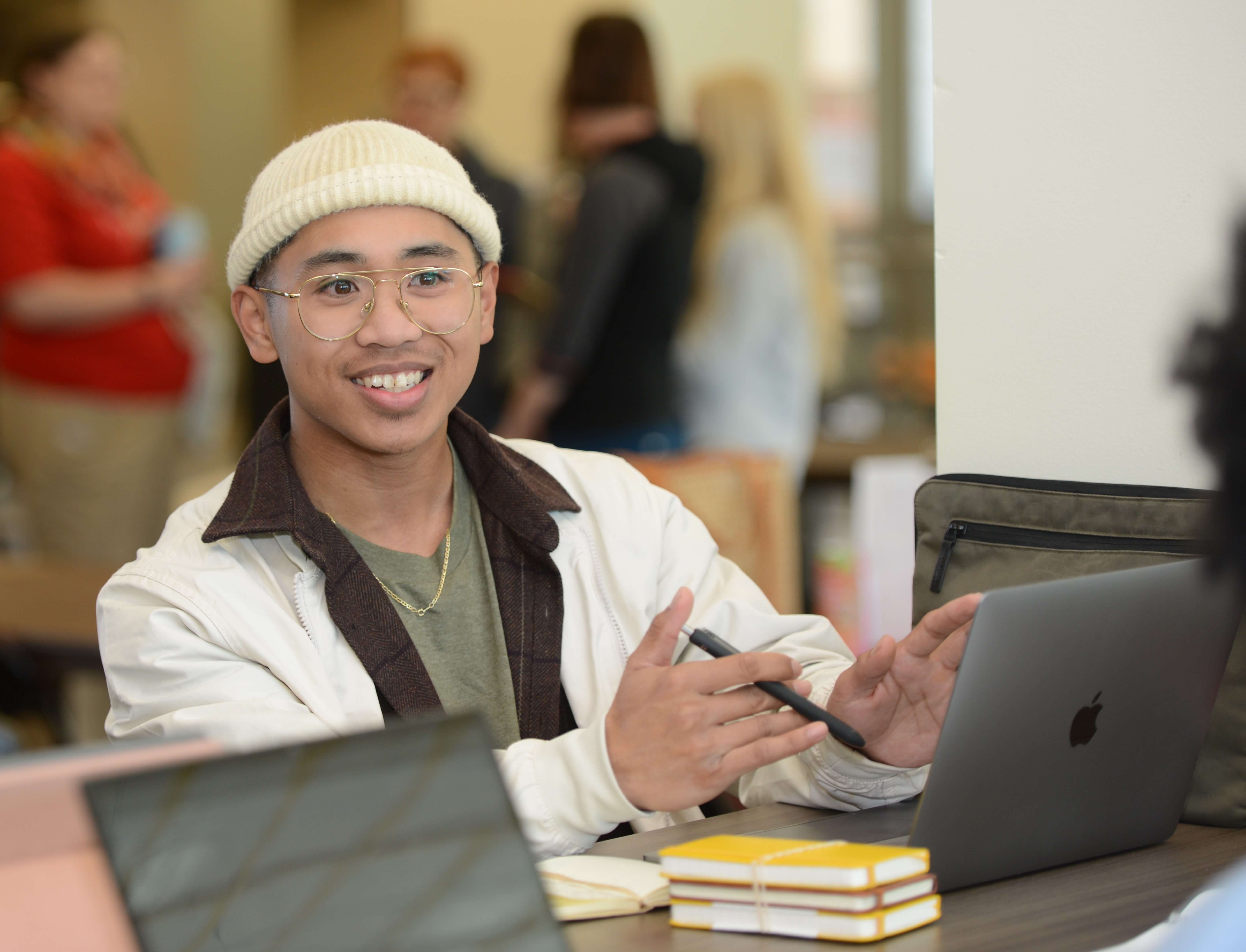 student sits at a table in common area with laptop