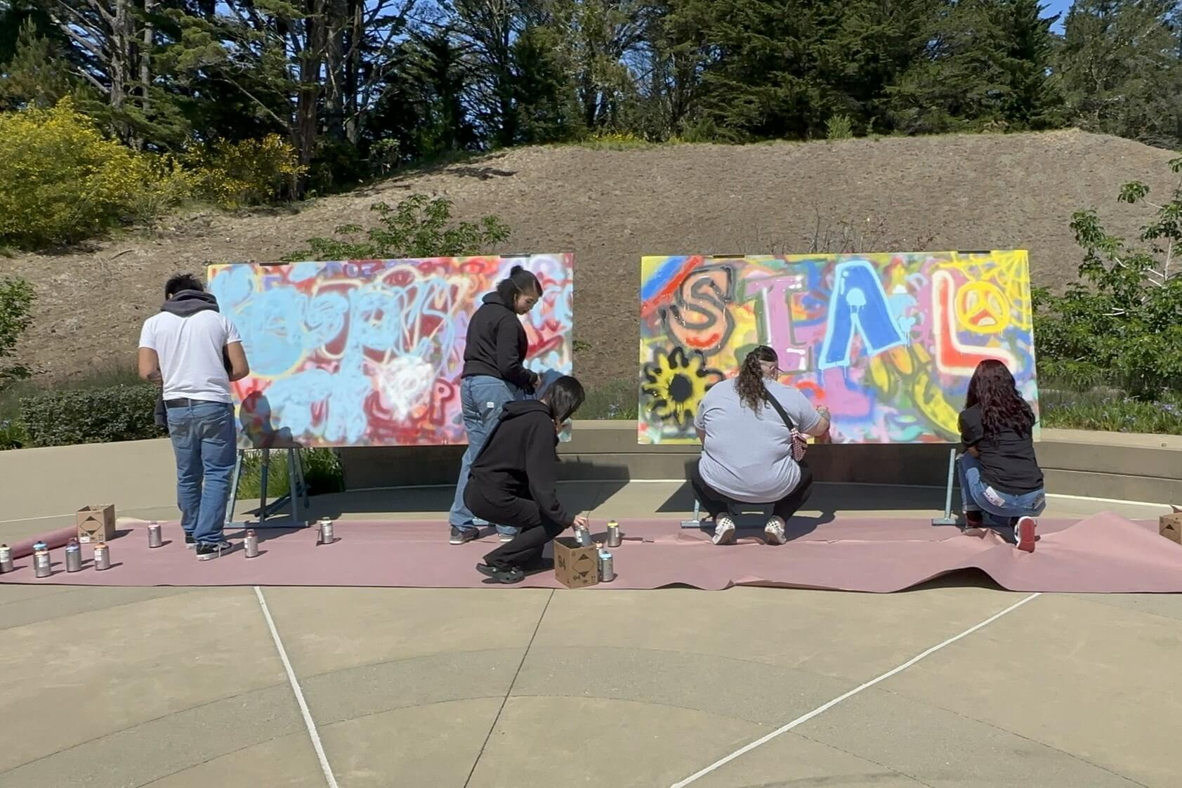 Rock the School Bells activity: students spray paint art on large easels outside