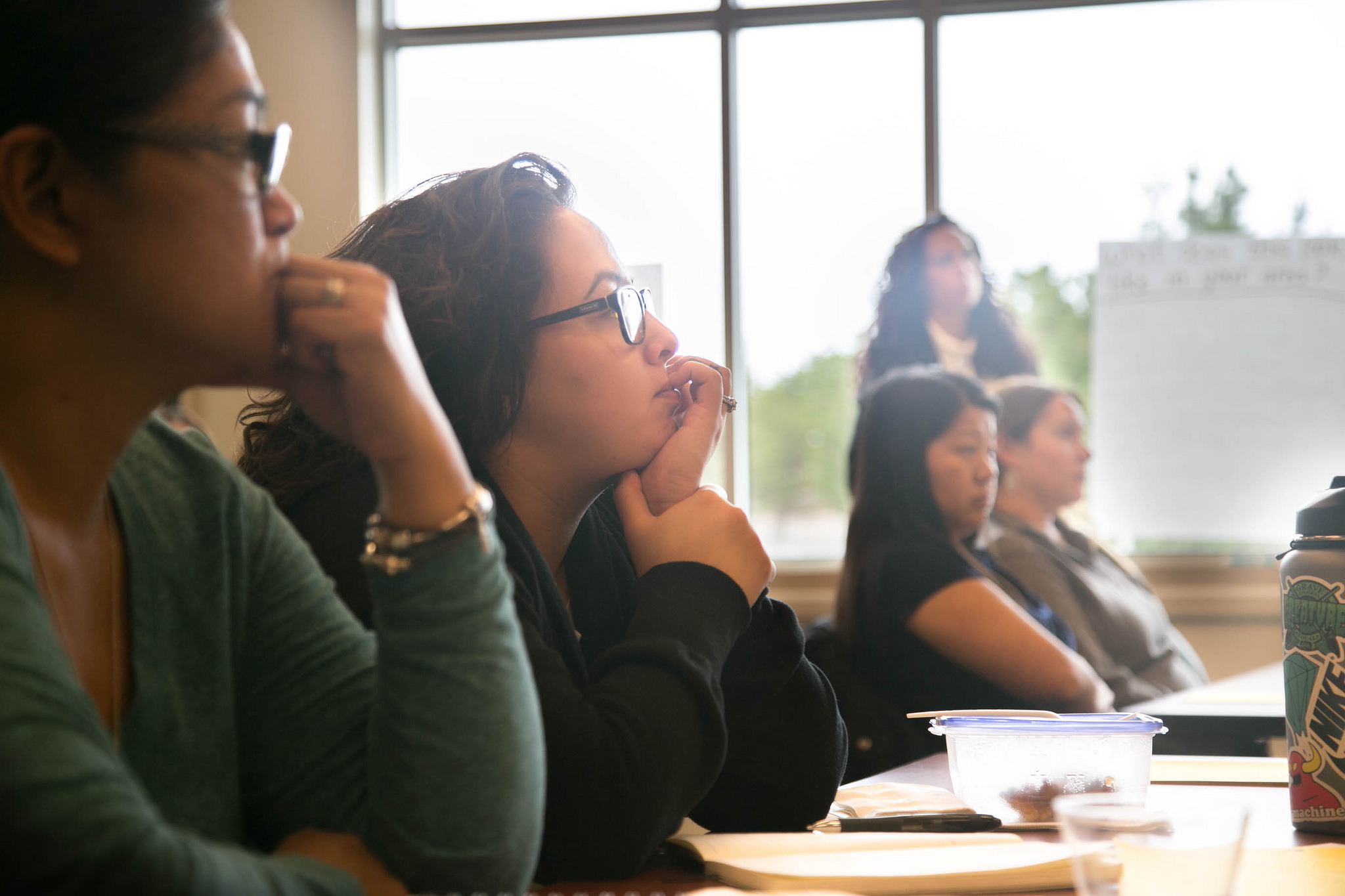 woman sits at a desk and listens to a presenter out of sight