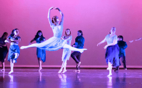 Onstage in purple lights, a group dances in unison