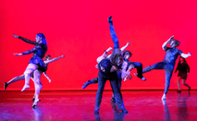 Onstage in pink light, a ballerina leaps across stage