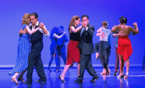 Onstage in blue lights, couples dance tango