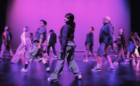 Onstage in red lights, dancers kick their legs behind them