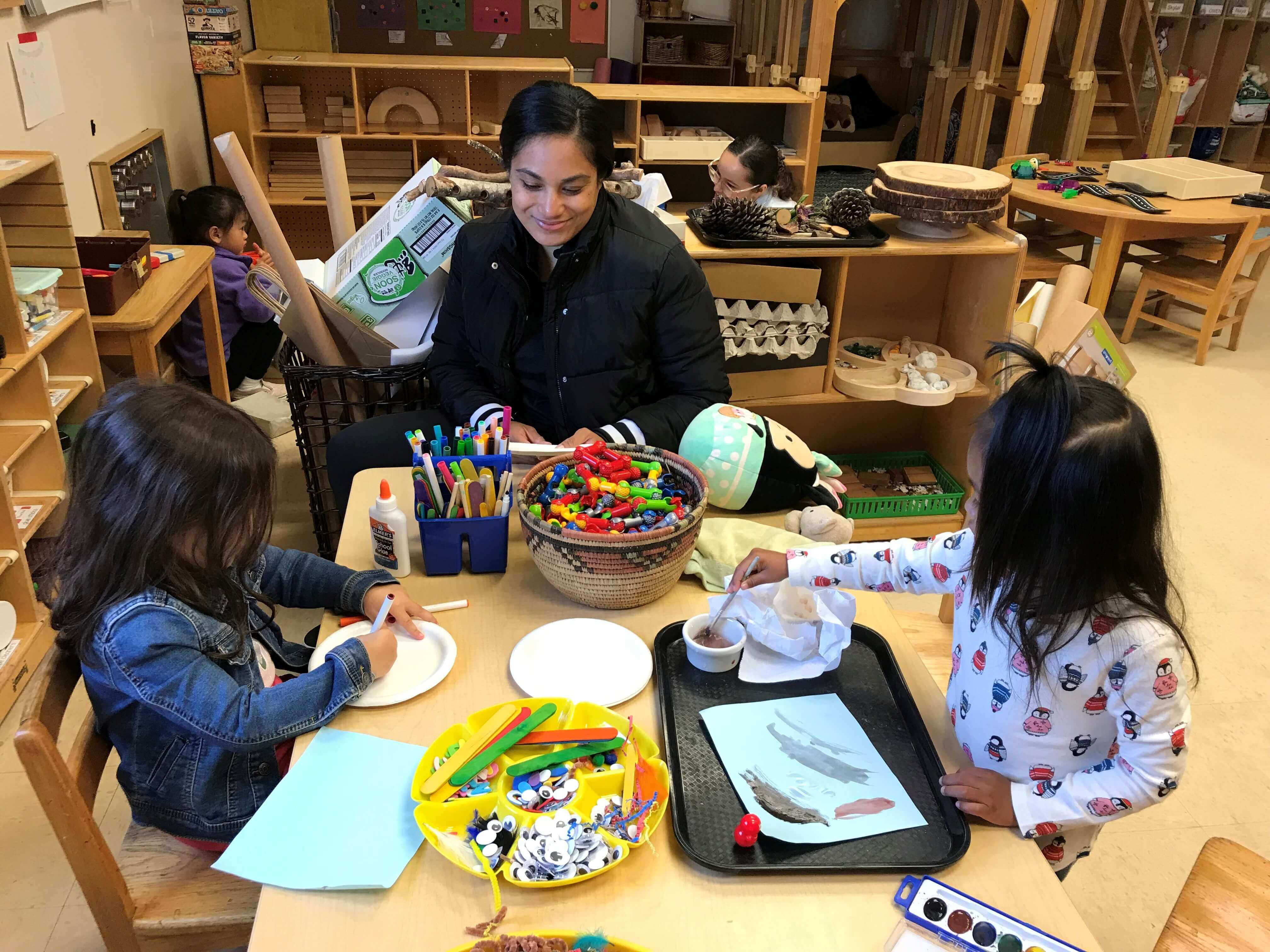 ECAP apprentice sits at a table with two young students who are coloring