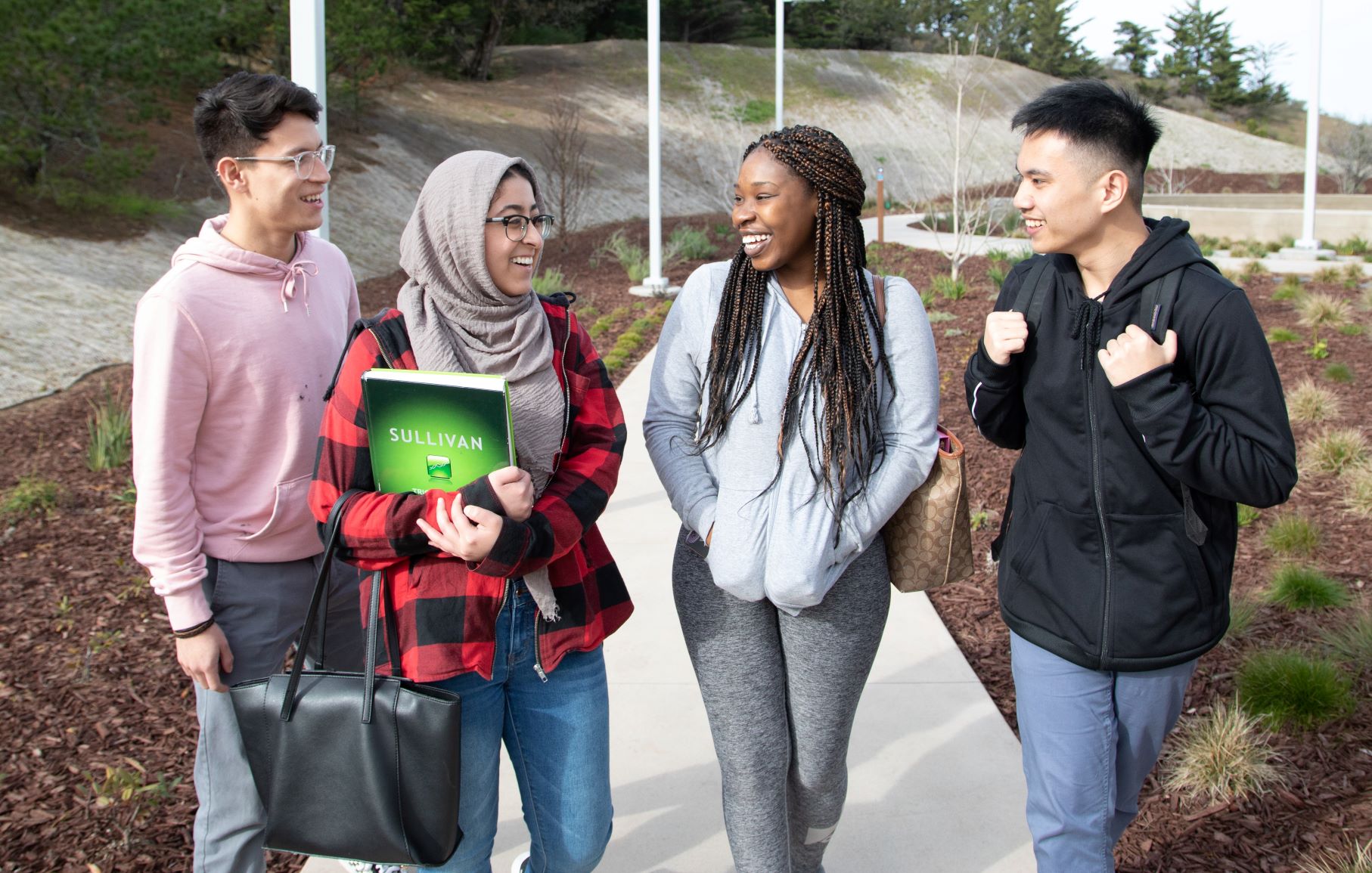 a group of 4 students wearing backpacks and carrying books walks down a path at Skyline College