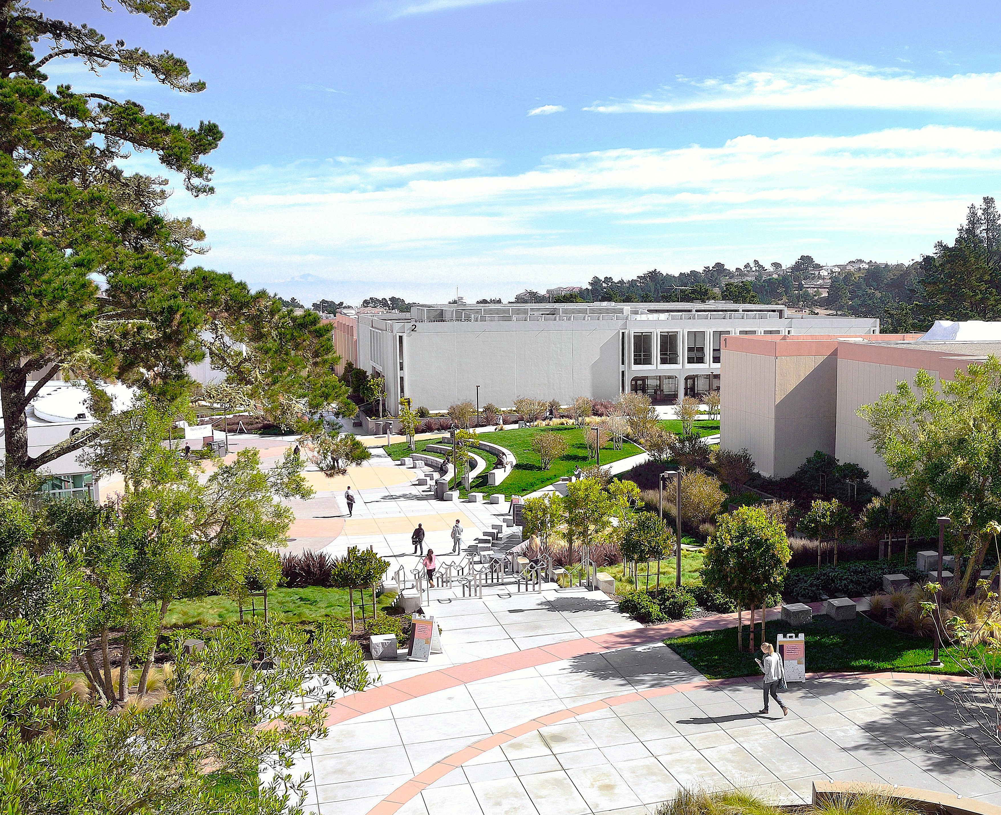 View of students walking up the stairs from the campus quad, with a tree in the foreground and blue skies overhead