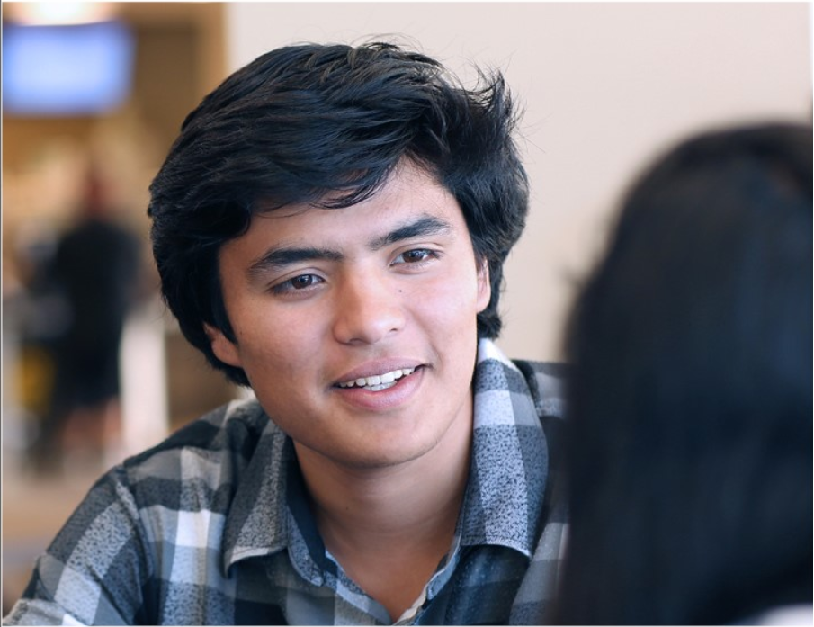Student in flannel shirt sits in campus cafe and talks to someone