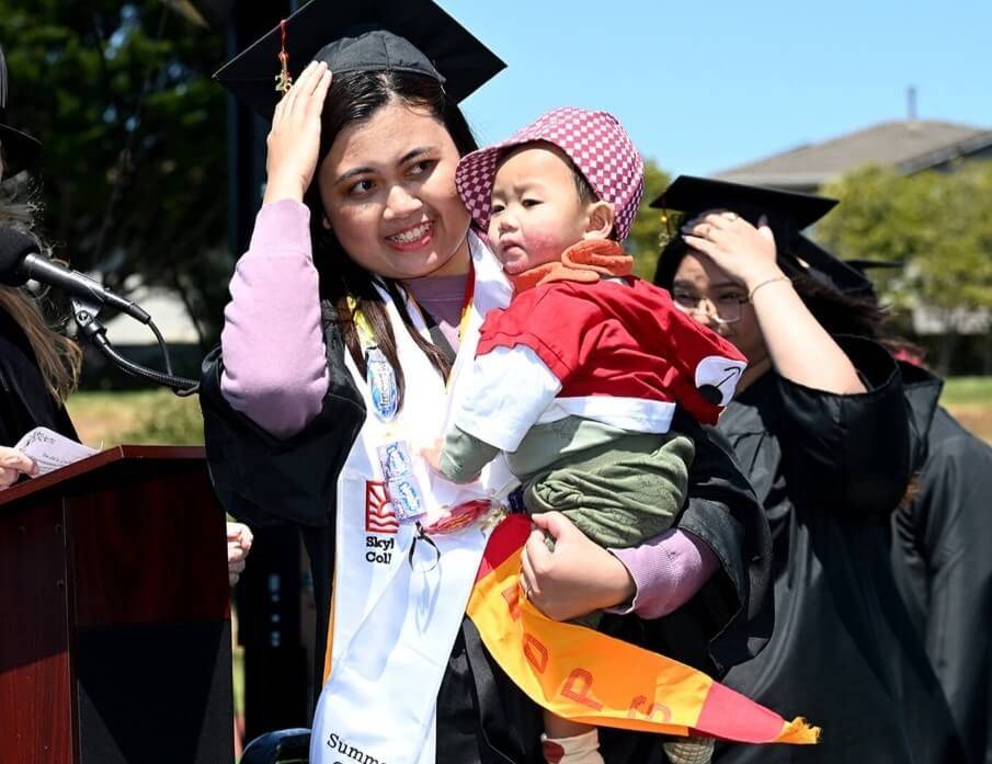 Student graduates and crosses the stage smiling and holding her baby