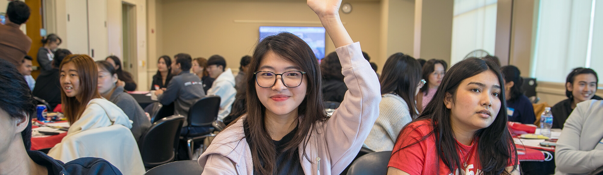 a student raises her hand and smiles in an outreach orientation