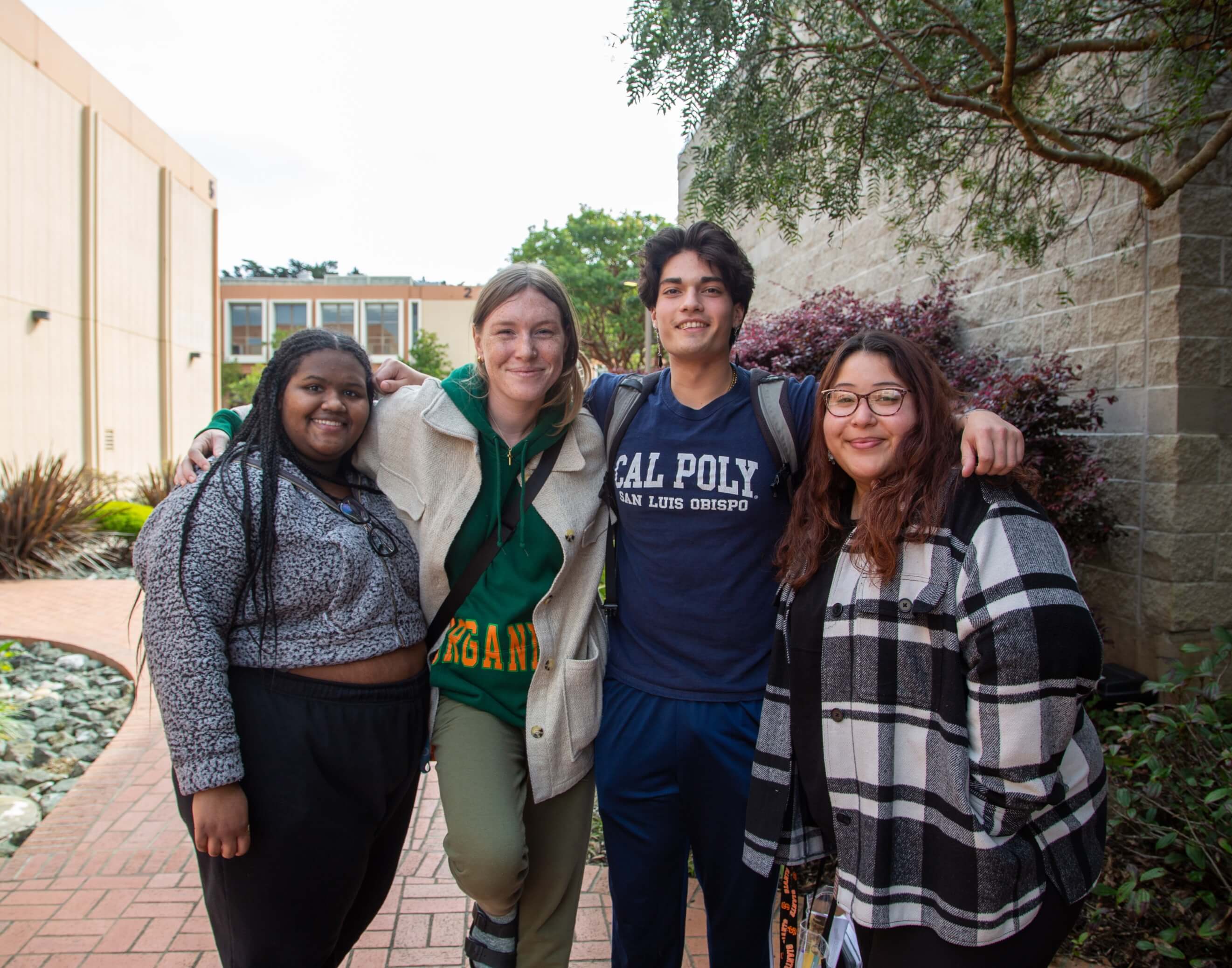 4 students smile in front of the entrance to the quad on campus