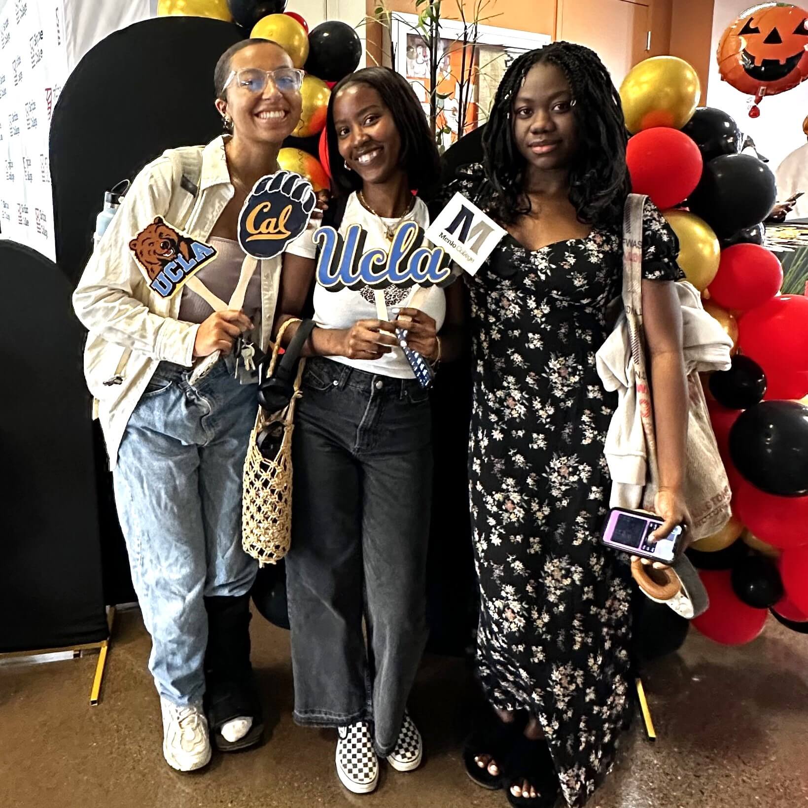 three students stand with hold-up signs of UCLA, Cal, and Menlo College at a Transfer Fair.